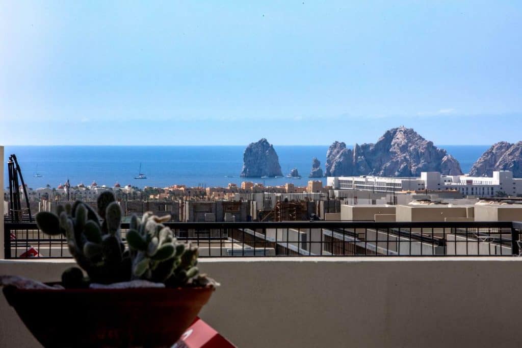 How To Buy Property In Pedregal Cabo: A Foreign Buyer’s Guide – Homes For Sale In Pedregal Breathtaking Pedregal View Of Cabo San Lucas Coastline With Sea Stacks And Boats From A Balcony With A Potted Cactus In The Foreground.