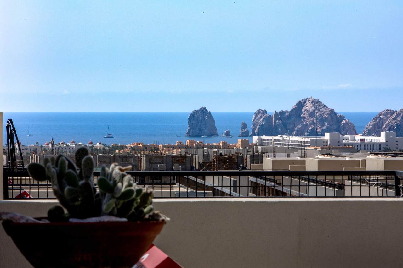 Breathtaking Pedregal View Of Cabo San Lucas Coastline With Sea Stacks And Boats From A Balcony With A Potted Cactus In The Foreground.