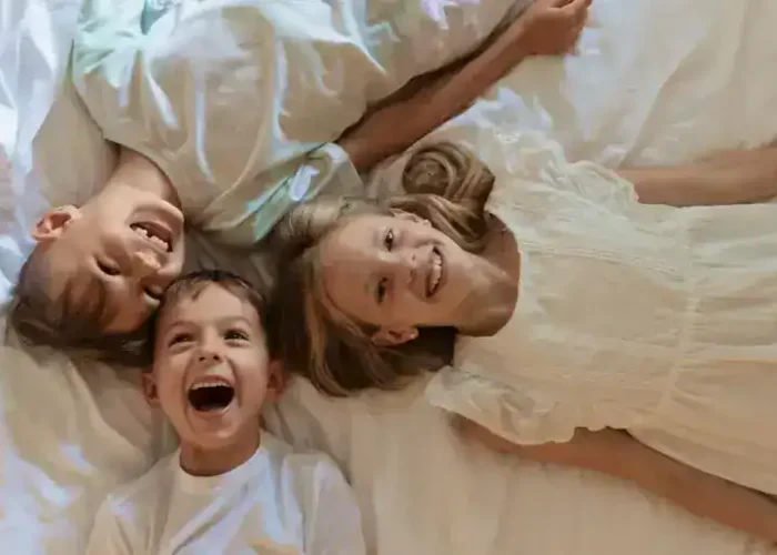 Family &Amp; Kids β Homes For Sale In Pedregal Joyful Family Enjoying A Playful Moment On A Bed In A Pedregal Home, Showcasing Comfort And Happiness In A Luxurious Real Estate Environment.
